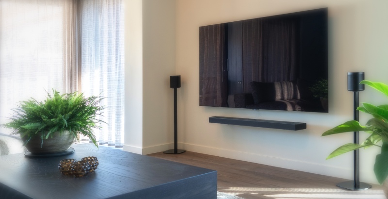 Een Televisie aan de muur met 2 speakers ernaast op speaker standaarden in de woonkamer