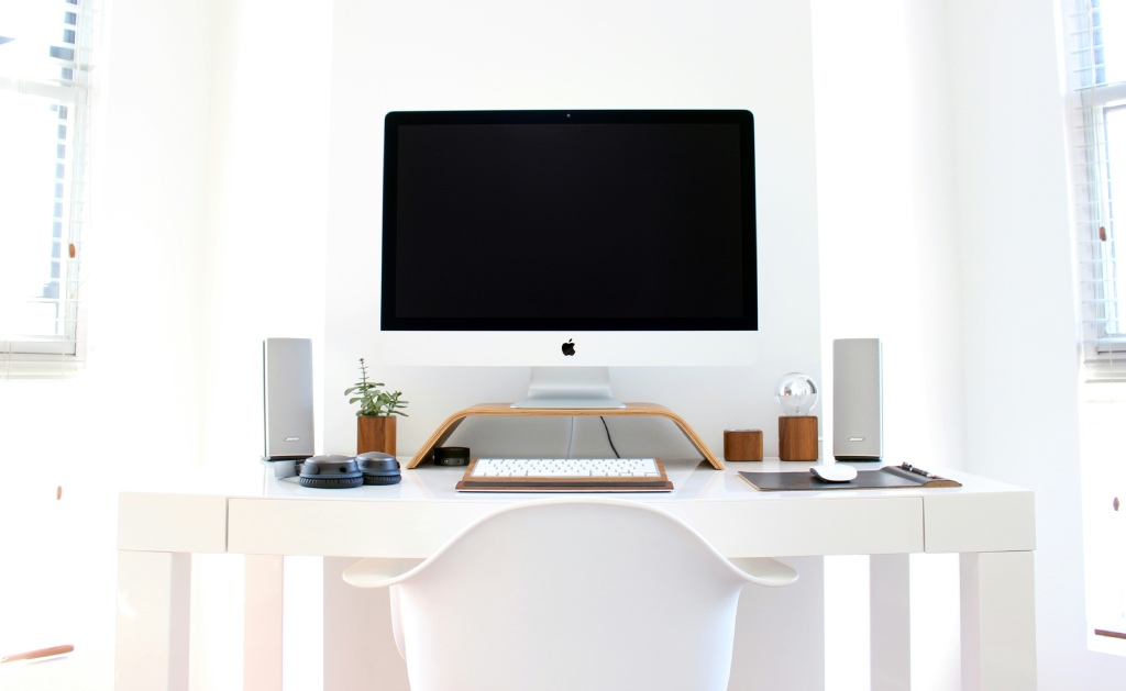 Een modern wit interieur met een bureau met een computer en twee speakers aan weerszijden